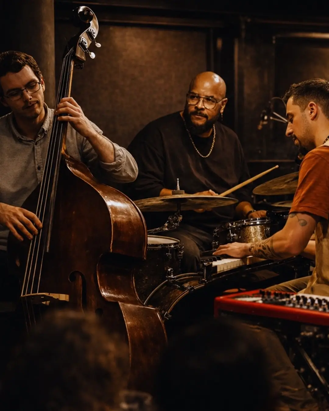 A jazz trio performs live in an intimate club setting, featuring piano, double bass, and drums, surrounded by warm lighting.