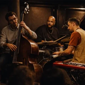 A jazz trio performs live in an intimate club setting, featuring piano, double bass, and drums, surrounded by warm lighting.