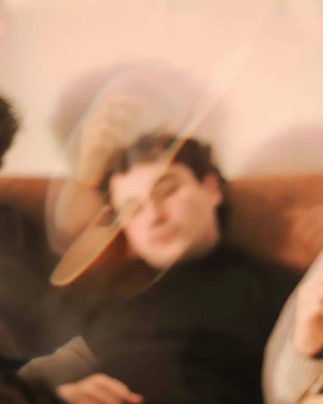 Three musicians sit together on a couch in a warm, dreamy, slightly blurred setting.