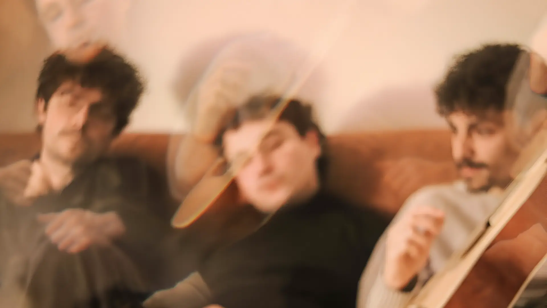 Three musicians sit together on a couch in a warm, dreamy, slightly blurred setting.