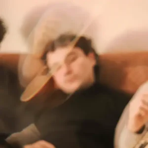 Three musicians sit together on a couch in a warm, dreamy, slightly blurred setting.