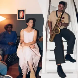 Saxofonist Mark Beebe zit op een trap en speelt terwijl mensen ontspannen in een huiselijke setting om hem heen zitten, sommigen luisterend en anderen met een drankje of telefoon in de hand.