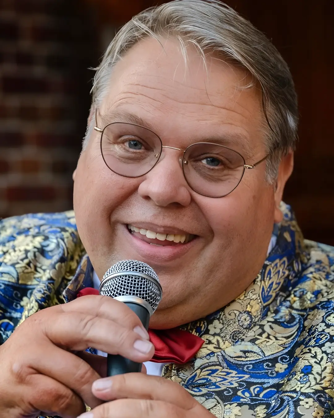 Portret van zanger Rico Parlevliet die glimlachend in een microfoon zingt, gekleed in een opvallend patroonjasje met strik, in een warme en intieme setting.