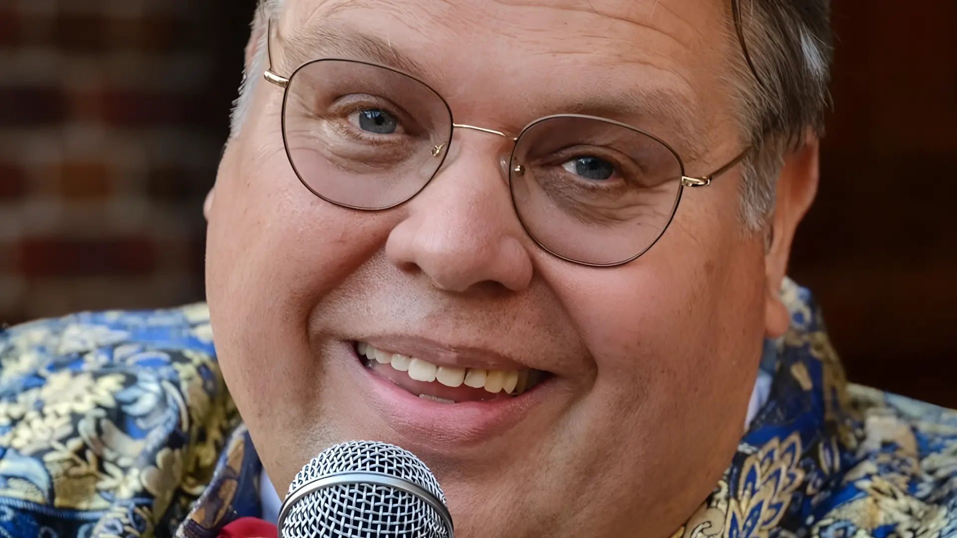 Portret van zanger Rico Parlevliet die glimlachend in een microfoon zingt, gekleed in een opvallend patroonjasje met strik, in een warme en intieme setting.