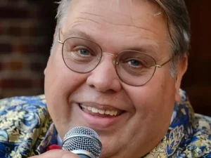 Portret van zanger Rico Parlevliet die glimlachend in een microfoon zingt, gekleed in een opvallend patroonjasje met strik, in een warme en intieme setting.