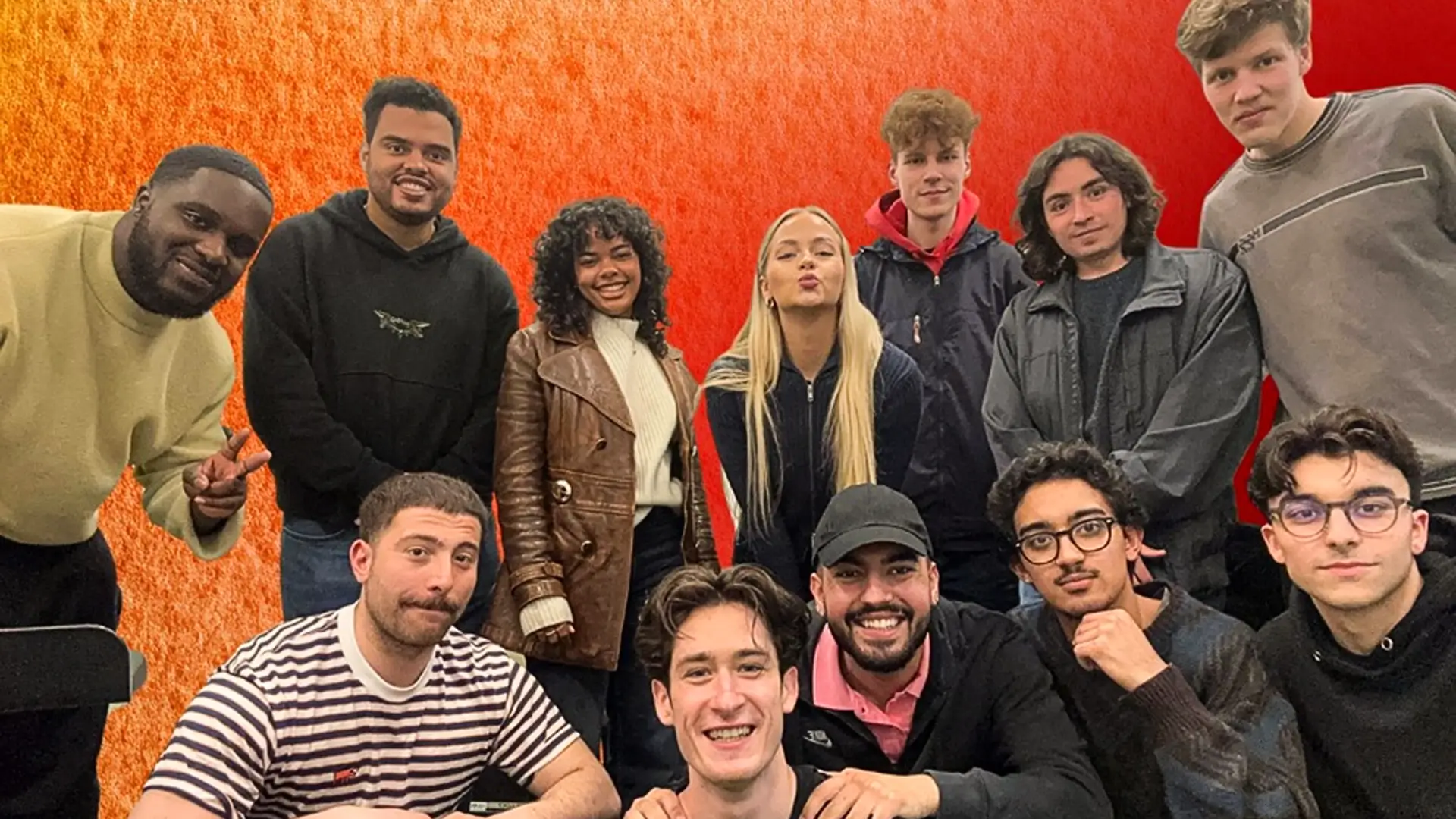 Een grote groep jonge muzikanten poseert samen voor een warme rood-oranje achtergrond, glimlachend en dicht bij elkaar, als bandfoto.