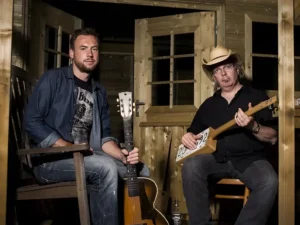 Gumbo & The Monk poseren met gitaren en een zelfgebouwde cigar box guitar in een houten, intieme setting, voorafgaand aan hun optreden tijdens Red Light Jazz.