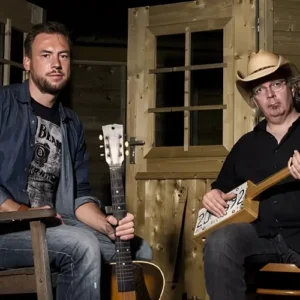 Gumbo & The Monk poseren met gitaren en een zelfgebouwde cigar box guitar in een houten, intieme setting, voorafgaand aan hun optreden tijdens Red Light Jazz.