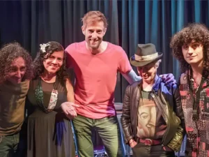 Vijf bandleden van Achha staan samen op het podium en poseren na een optreden.