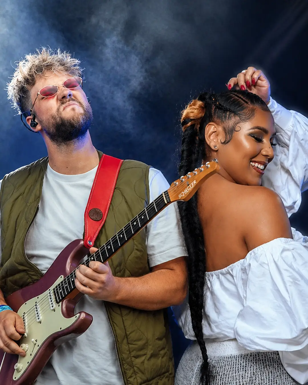 Lorijn van Piekartz speelt elektrische gitaar op het podium naast zangeres Cheyenne Toney, die glimlachend danst, onder helder podiumlicht met een donkere achtergrond.