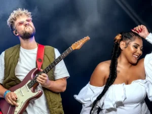 Lorijn van Piekartz speelt elektrische gitaar op het podium naast zangeres Cheyenne Toney, die glimlachend danst, onder helder podiumlicht met een donkere achtergrond.