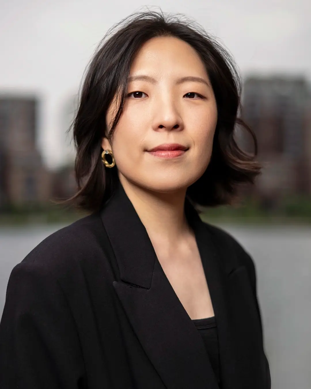 Zwart-wit portret van jazzpianiste Miran Noh, frontaal kijkend, met een rustige en zelfverzekerde uitstraling tegen een zacht vervaagde stedelijke achtergrond.