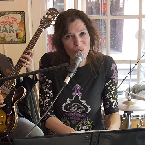 Ruth Geerse zingt en speelt piano tijdens een live optreden in een intieme setting, begeleid door een gitarist en drummer.
