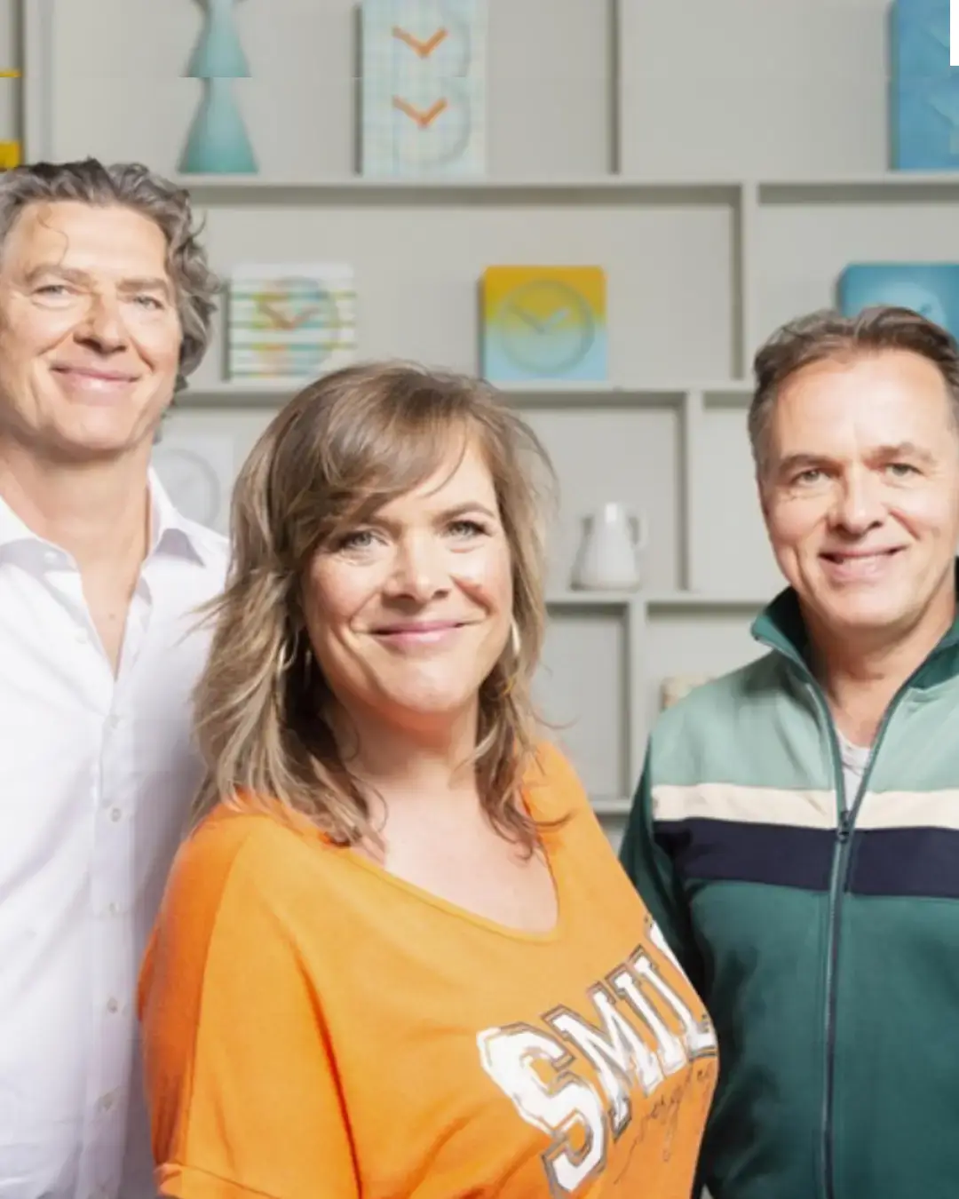 Drie muzikanten van Something About Sanna poseren samen en kijken glimlachend in de camera.