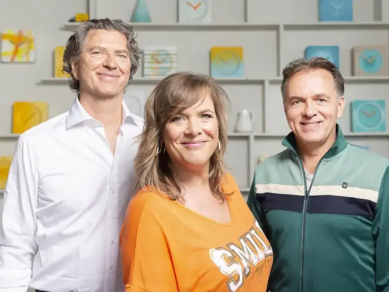 Drie muzikanten van Something About Sanna poseren samen en kijken glimlachend in de camera.