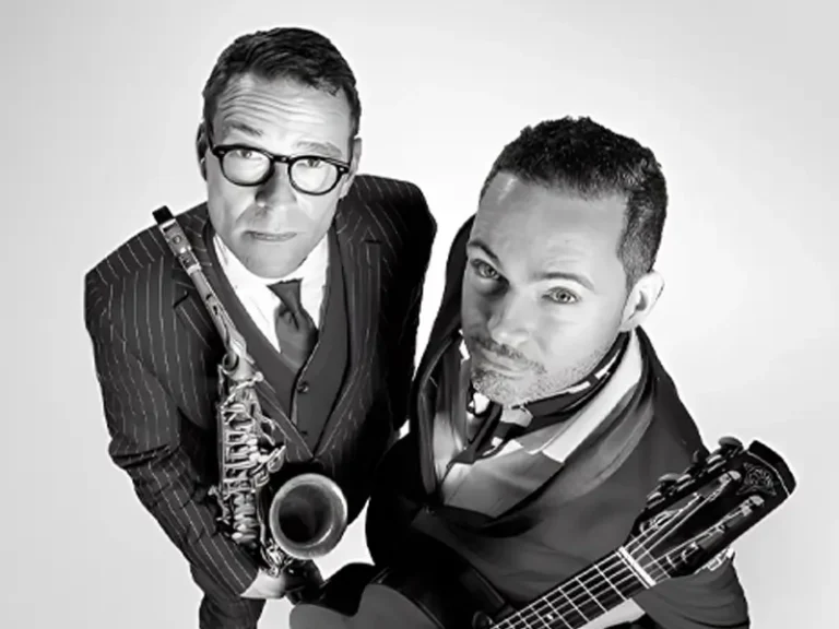 Zwart-wit portret van Benjamin Herman en Robin Nolan die omhoog in de camera kijken; links een saxofonist in pak met bril die zijn instrument vasthoudt, rechts een gitarist met een gitaar, beiden strak gekleed en close bij elkaar in beeld.