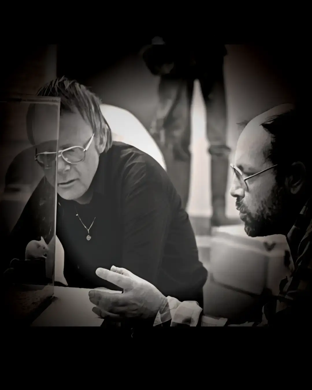 Zwart-wit foto van Misha Mengelberg & Louis Andriessen: Goede Maten die geconcentreerd kijken naar een glazen vitrine met een kleine installatie, terwijl ze met elkaar in gesprek zijn.