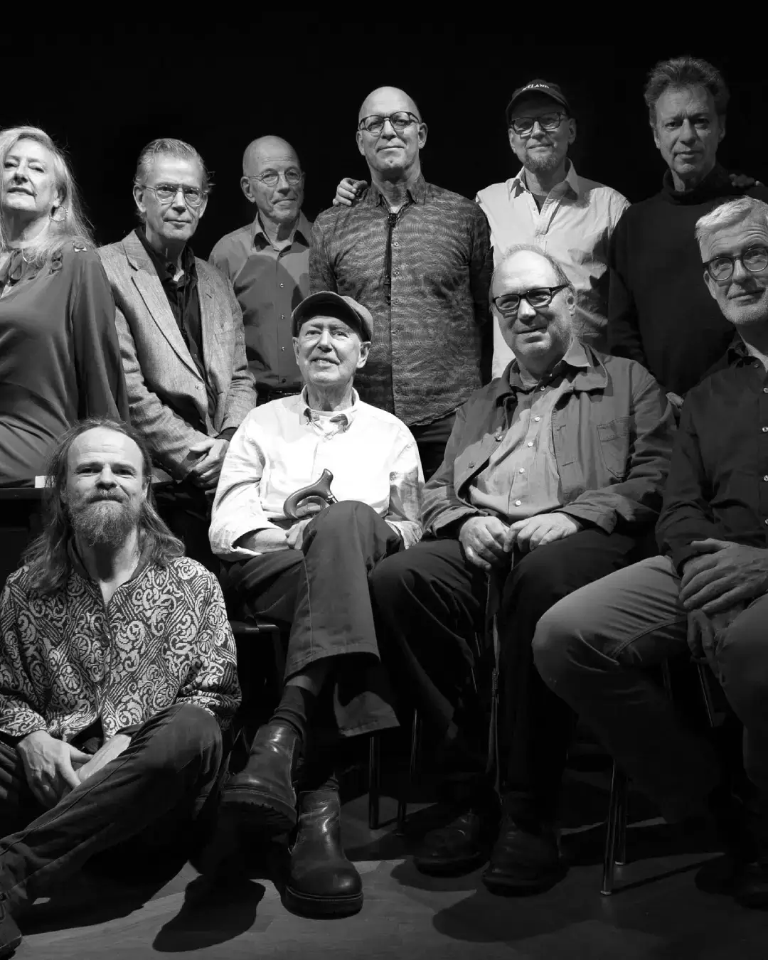 Zwart-wit groepsportret van IPC Orchestra een groot jazzensemble met mannen en één vrouw, zittend en staand op een podium tegen een donkere achtergrond.