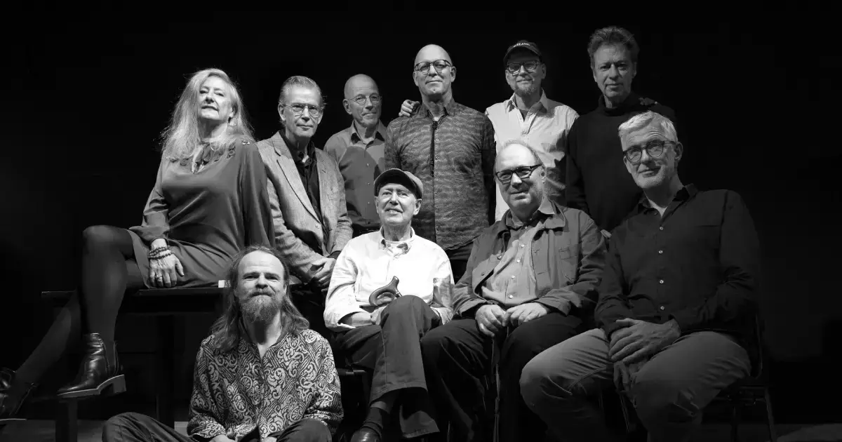 Zwart-wit groepsportret van IPC Orchestra een groot jazzensemble met mannen en één vrouw, zittend en staand op een podium tegen een donkere achtergrond.