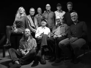 Zwart-wit groepsportret van IPC Orchestra een groot jazzensemble met mannen en één vrouw, zittend en staand op een podium tegen een donkere achtergrond.