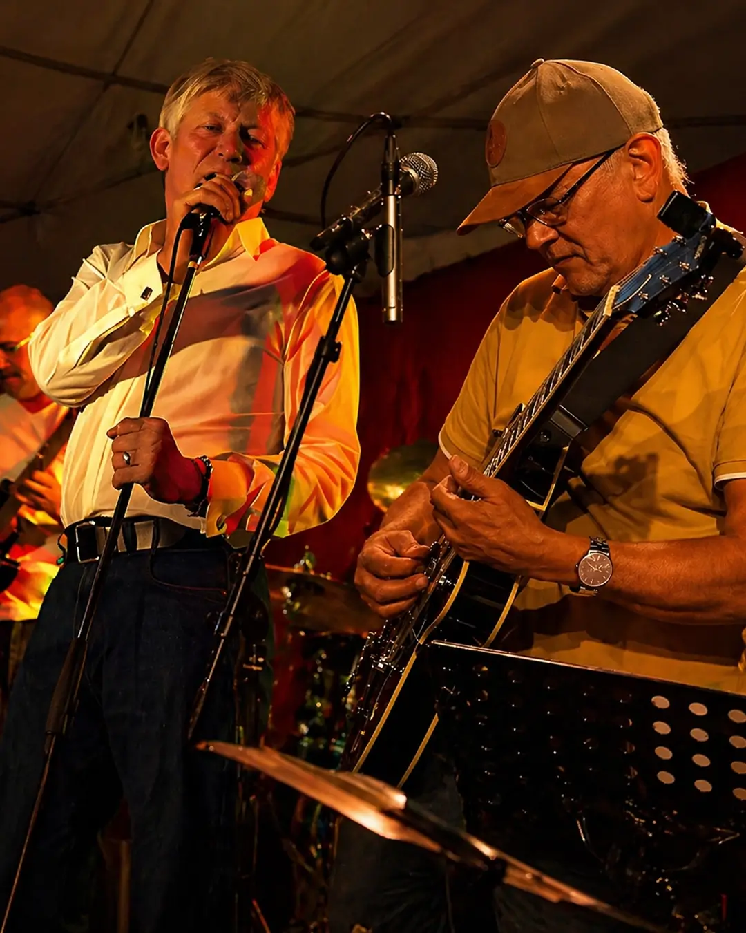 Twee muzikanten treden live op onder warm podiumlicht: zanger Andre Moehijam zingt in de microfoon terwijl gitarist Janne Buurman (Jay Bee Silverfox) geconcentreerd gitaar speelt, met een drumstel op de achtergrond.