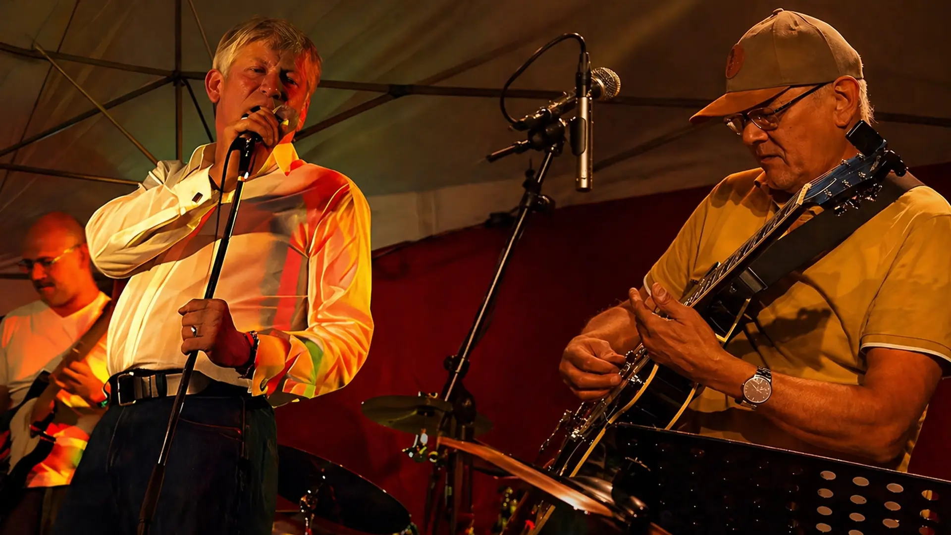Twee muzikanten treden live op onder warm podiumlicht: zanger Andre Moehijam zingt in de microfoon terwijl gitarist Janne Buurman (Jay Bee Silverfox) geconcentreerd gitaar speelt, met een drumstel op de achtergrond.