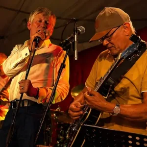 Twee muzikanten treden live op onder warm podiumlicht: zanger Andre Moehijam zingt in de microfoon terwijl gitarist Janne Buurman (Jay Bee Silverfox) geconcentreerd gitaar speelt, met een drumstel op de achtergrond.