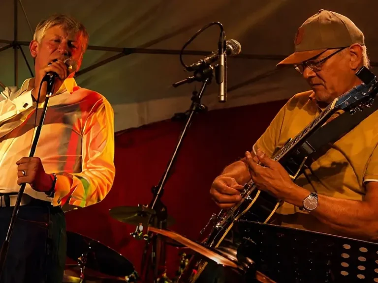 Twee muzikanten treden live op onder warm podiumlicht: zanger Andre Moehijam zingt in de microfoon terwijl gitarist Janne Buurman (Jay Bee Silverfox) geconcentreerd gitaar speelt, met een drumstel op de achtergrond.