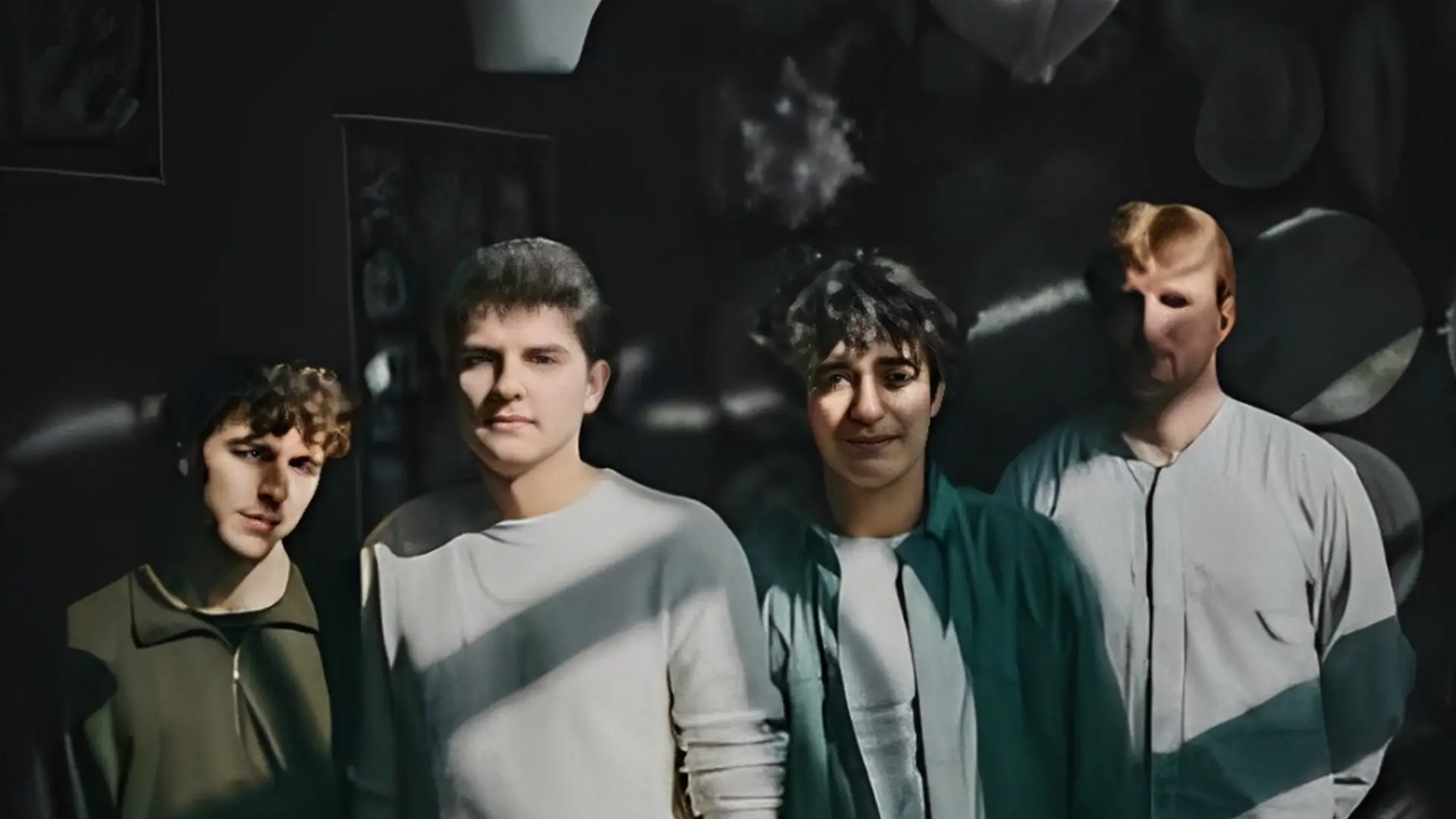 Vier jonge muzikanten staan samen in half schaduw en zonlicht, kijkend naar de camera, met een donkere achtergrond en sterke contrasten.