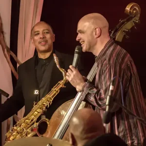 Saxofonist en bassist van Trio of Liberty staan samen op het podium en maken contact tijdens een live optreden.