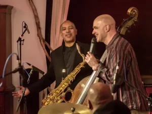 Saxofonist en bassist van Trio of Liberty staan samen op het podium en maken contact tijdens een live optreden.