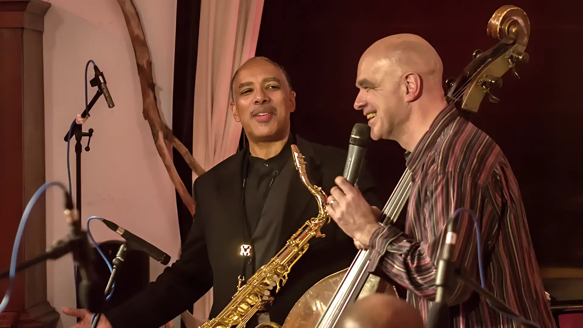 Saxofonist en bassist van Trio of Liberty staan samen op het podium en maken contact tijdens een live optreden.