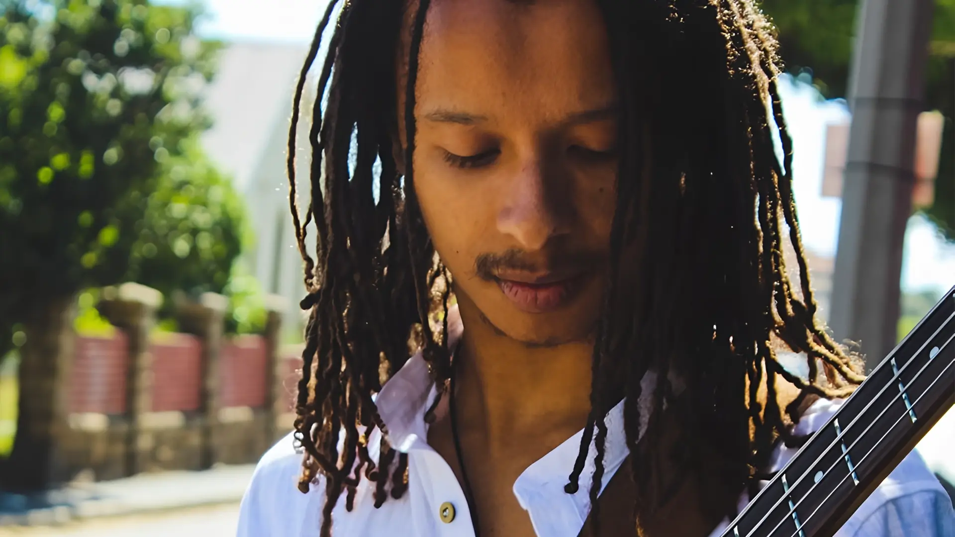 Bassist Zelzele met lange dreadlocks kijkt geconcentreerd naar zijn instrument terwijl hij buiten in het zonlicht speelt.